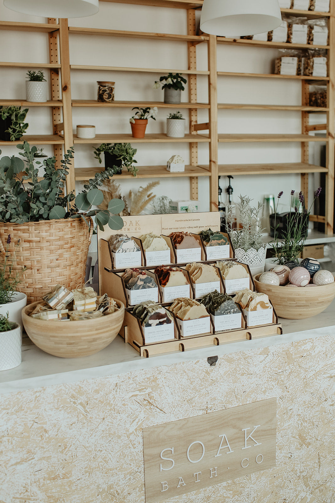 Display of soaps and bath products on a counter with shelves in the background, featuring the brand 'Soak Bath Co'.