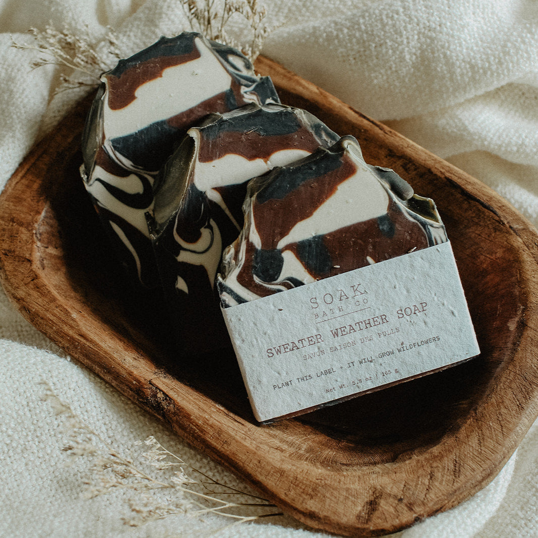 Three soap bars with a decorative pattern in a wooden dish on a white fabric background