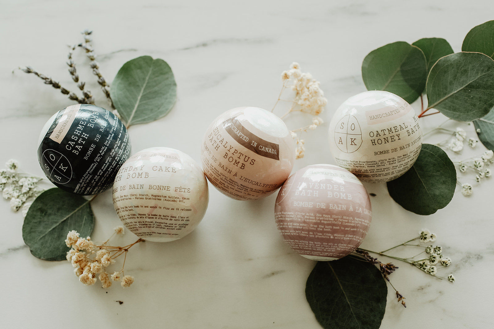 Bath bombs with labels on a marble surface with green leaves and flowers