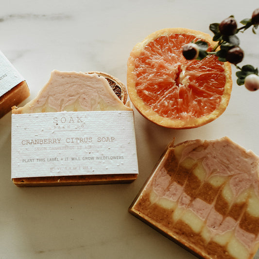 Three bars of soap with visible branding on a marble surface with dried oranges and flowers.