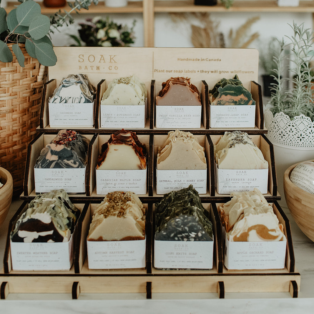 Display of soap bars in boxes with a wooden shelf and plants in the background