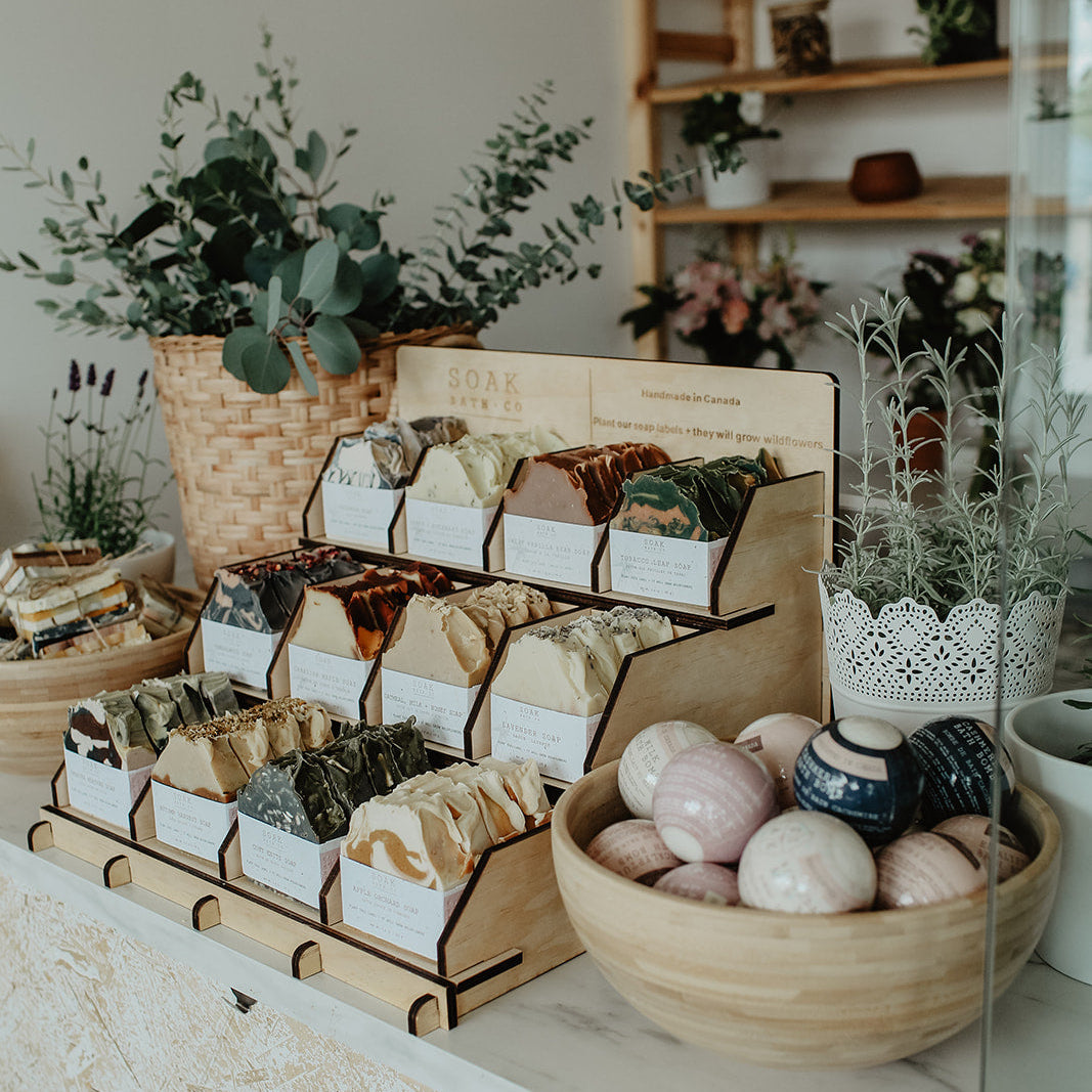Display of soaps and natural products in a store setting with plants and shelves.