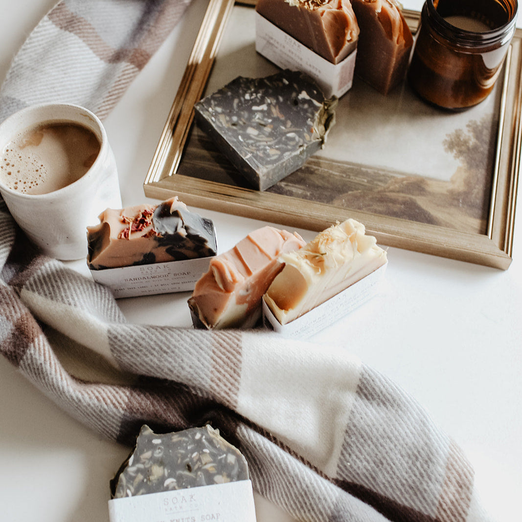 Assorted soaps on a wooden tray with a cup of coffee and plaid blanket.
