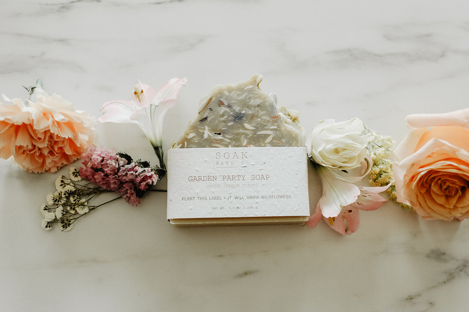 Bar of soap with a label surrounded by flowers on a marble surface