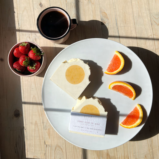 Breakfast setting with soap bar, fruit, and coffee on a wooden table