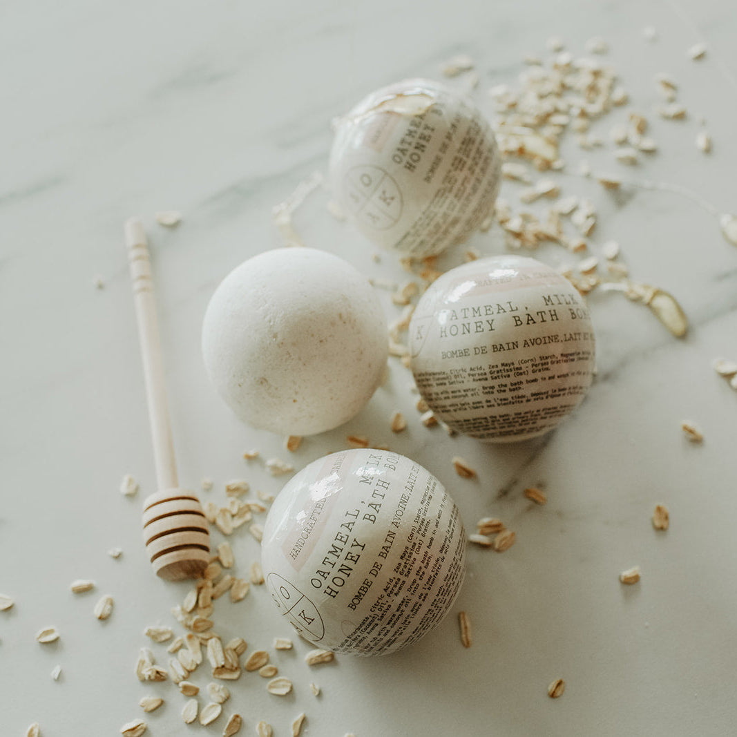 oatmeal, milk + honey bath bombs with text on a light marble surface with small shells.