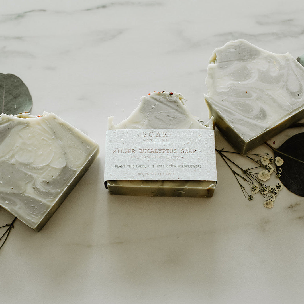 Three bars of soap with eucalyptus leaves on a marble surface