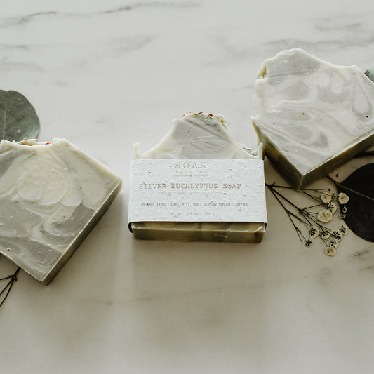 Three bars of soap with eucalyptus leaves on a marble surface