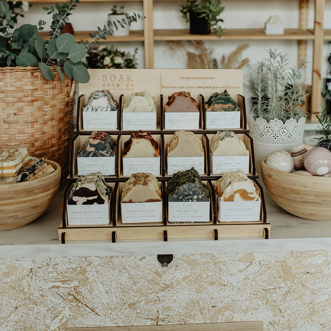 Display of soap bars in a wooden stand with 'SOAK BATH CO' branding, set against a wooden shelf background.