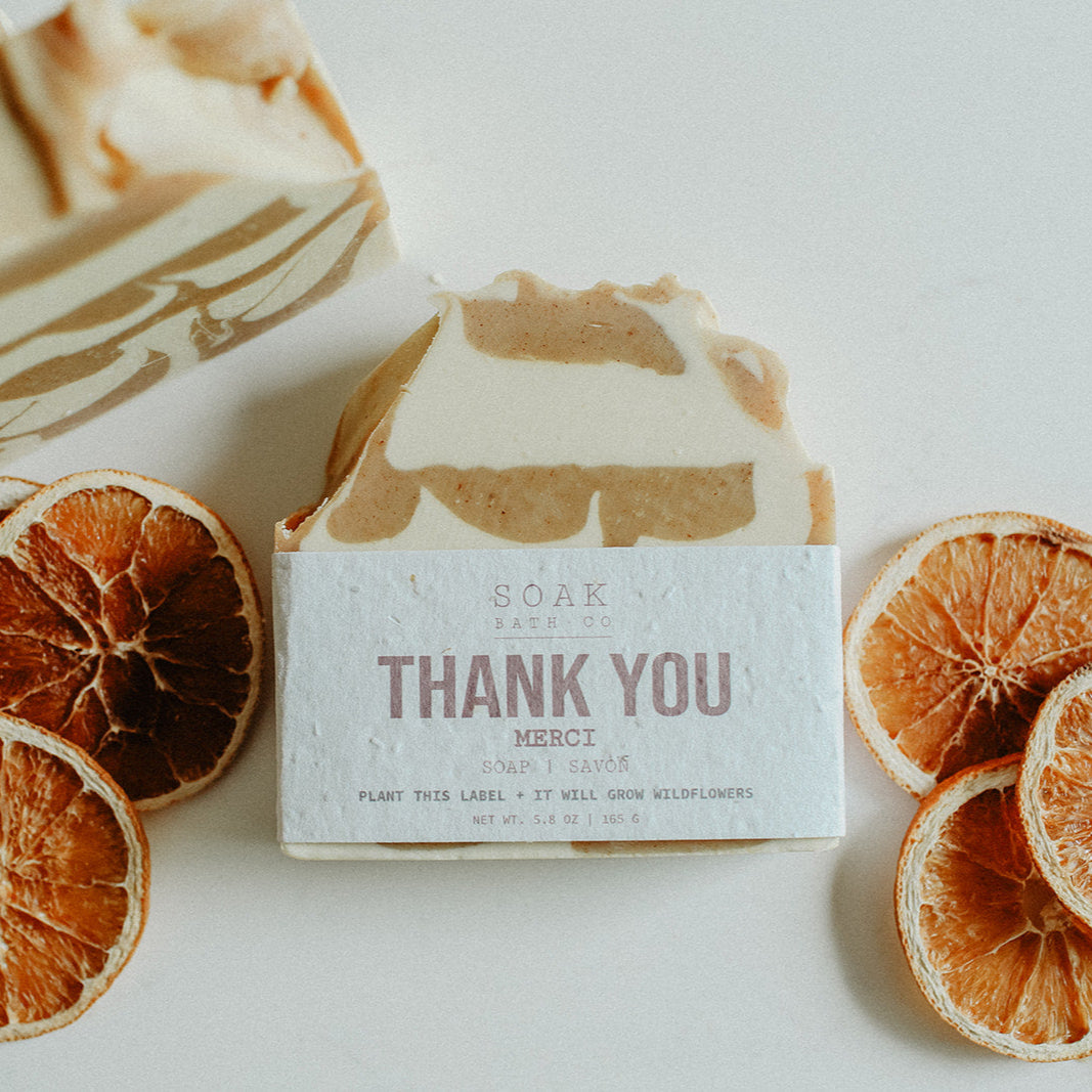 Bar of soap with a 'Thank You' message surrounded by dried orange slices on a light background