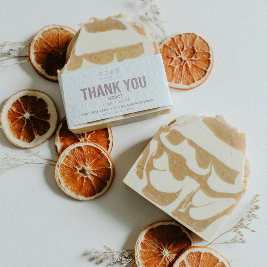 Two bars of soap with decorative packaging surrounded by dried orange slices on a light background