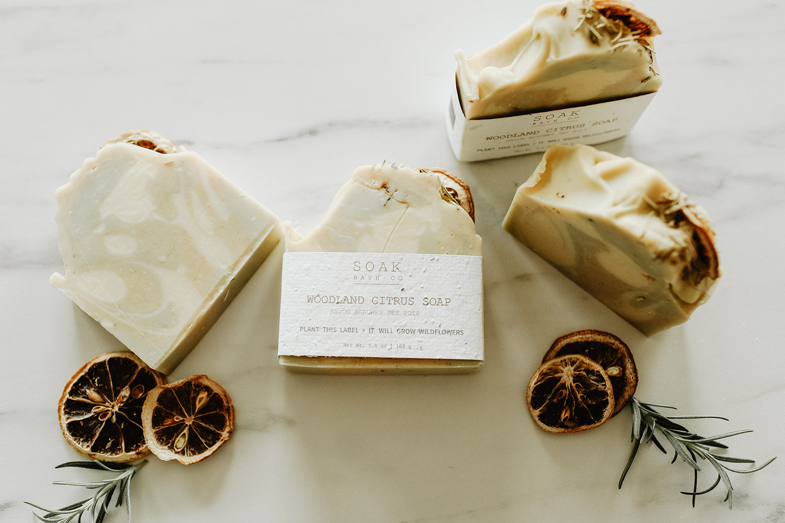 Three bars of soap on a marble surface with dried oranges and rosemary.